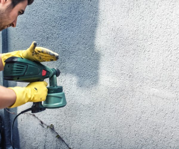 Man painting a grey wall, renovating exterior walls of new house
