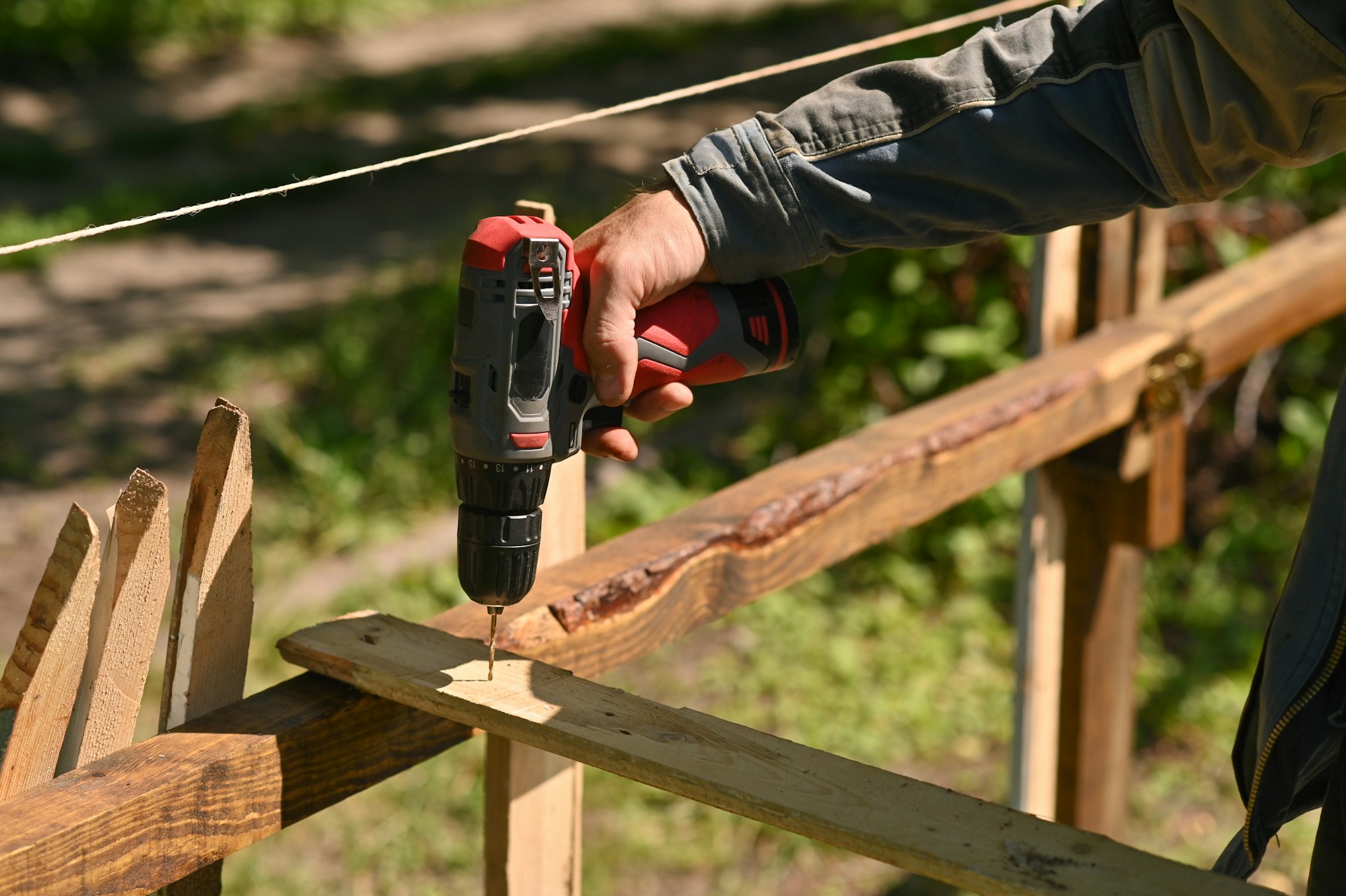 A man drills a hole in a wooden board. Making a fence in the garden.